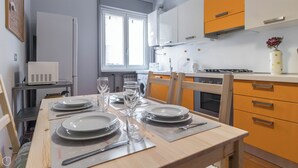 A dining table set with plates, glasses, and cutlery in a modern kitchen with wooden chairs and orange cabinets. - Italianway Easy - Sanfelice 10 (Milan)