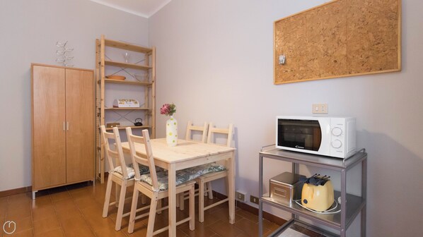Uma cozinha pequena com uma mesa de madeira, cadeiras, micro-ondas, torradeira, armário e um mural na parede.