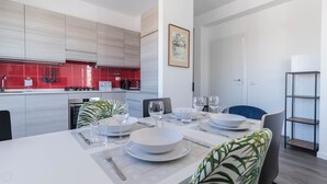A modern kitchen with red tiles, a dining area with a table set for four, and a bookshelf. - Italianway - Boiardo 27 (Milan)