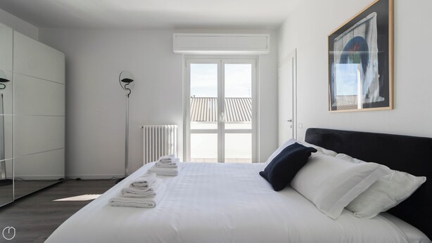 A bedroom with a large bed, a radiator, a floor lamp, and a window with a view of a balcony. - Italianway - Boiardo 27 (Milan)