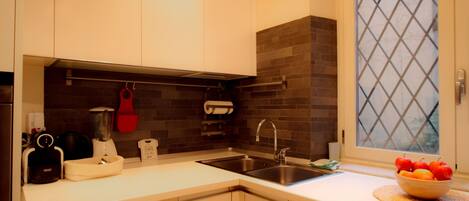 A modern kitchen with white cabinets, a stainless steel sink, and a window with a diamond-patterned blind.