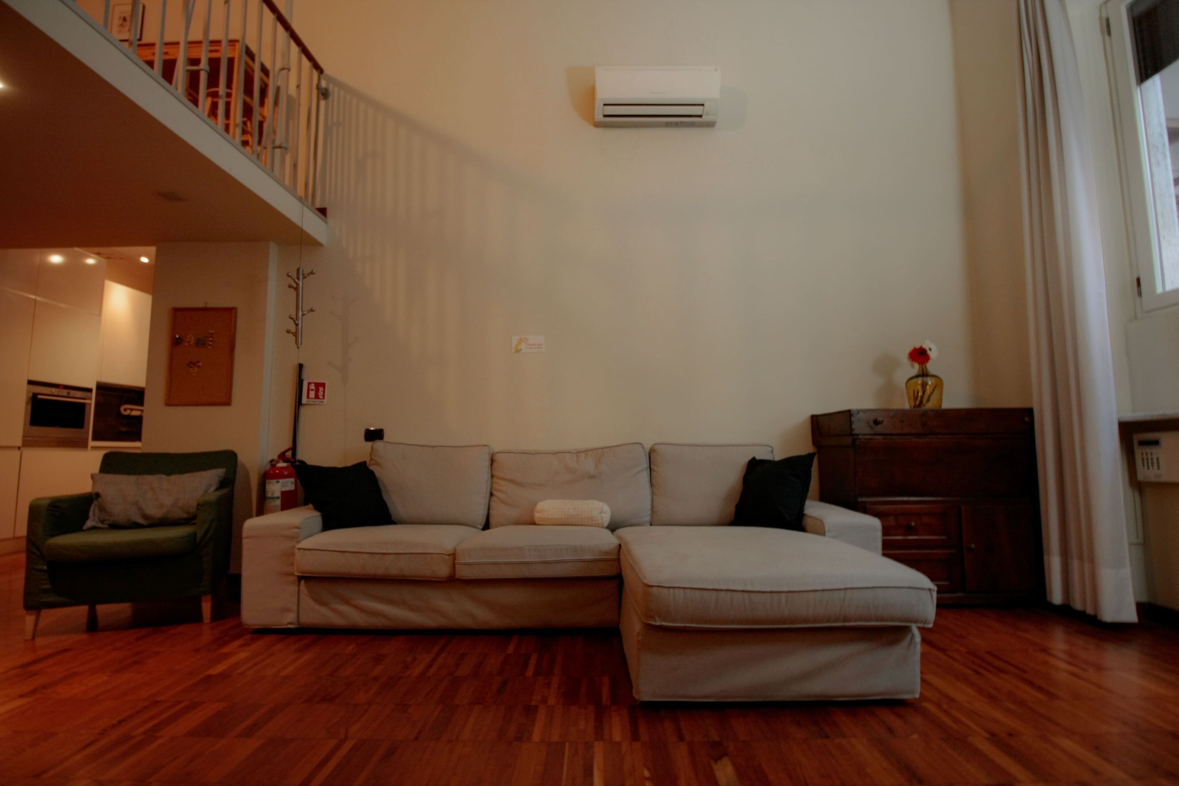 Ein Wohnzimmer mit einer Couch, einem Sessel, Holzboden, einer Treppe und einer Wandklimaanlage.