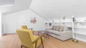 A modern living room with a white sofa, a yellow armchair, and a coffee table. There are bookshelves and a floor lamp.