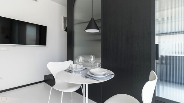 Un espace repas moderne avec une table ronde, des chaises blanches et un luminaire suspendu noir.