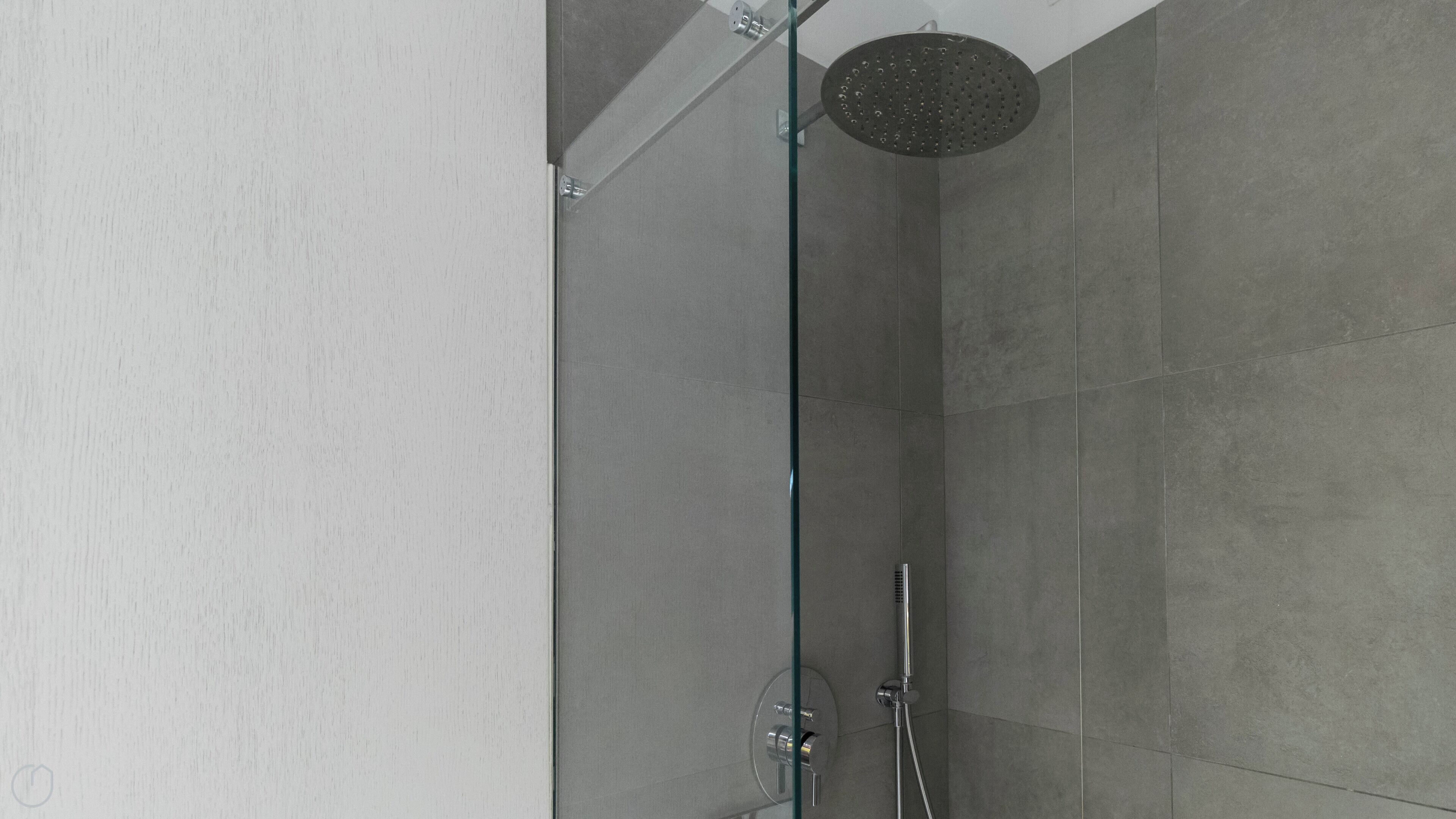 A modern shower with a glass door, a handheld showerhead, and a wall-mounted faucet.