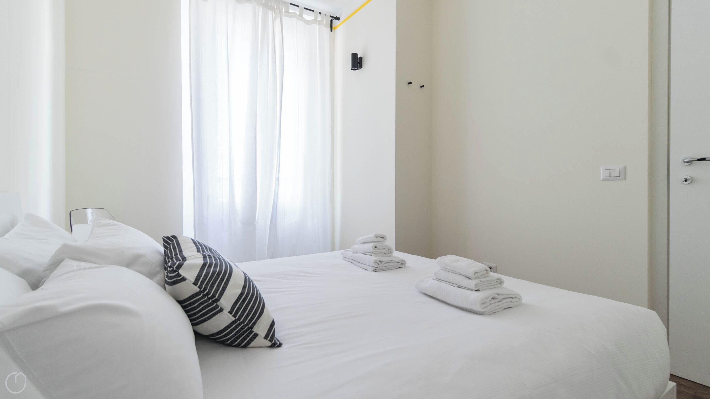 A hotel room with a neatly made bed, a striped pillow, and folded towels on the bed.