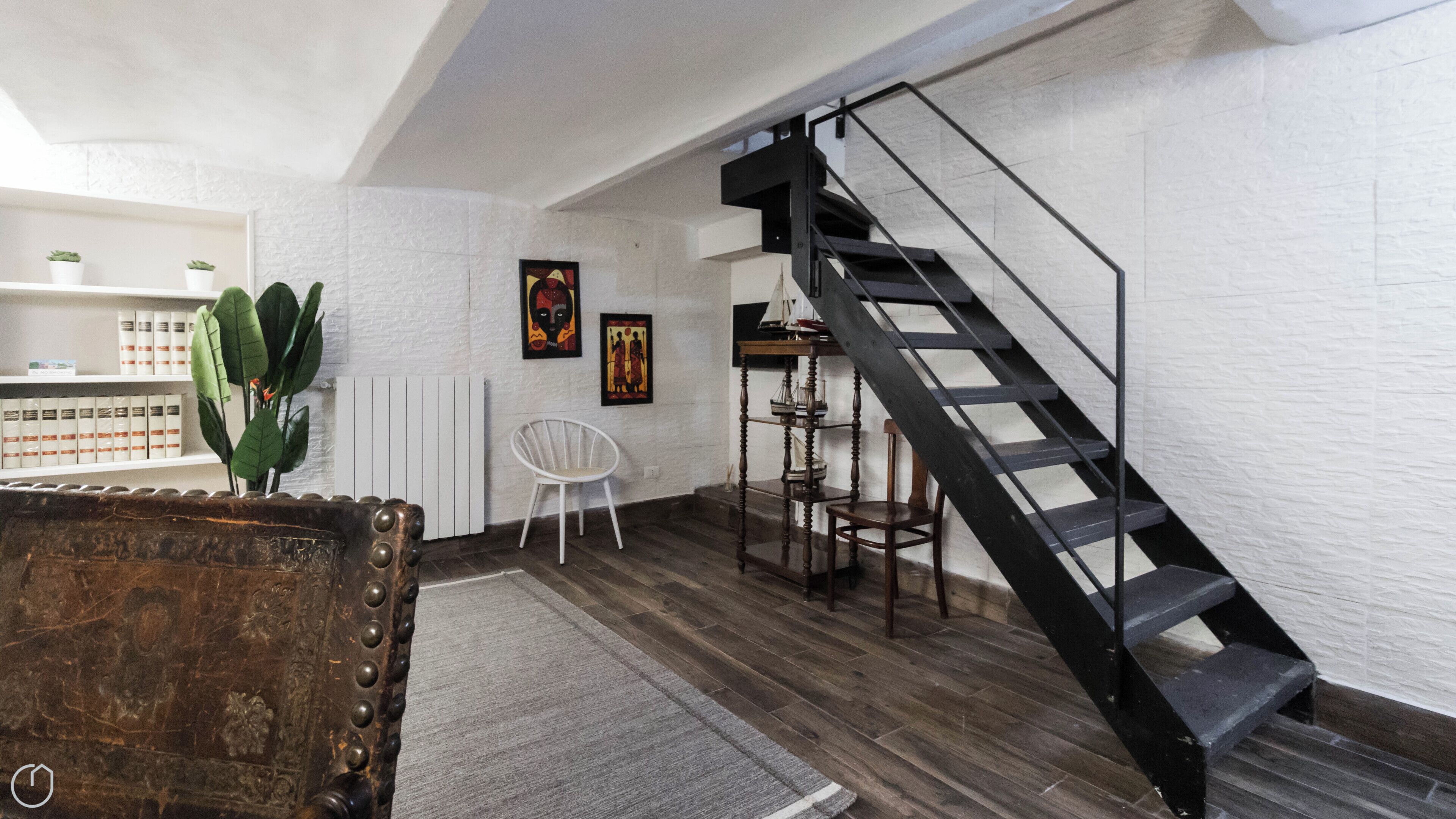 Un interior moderno con una escalera de madera, paredes blancas y una planta de cactus.