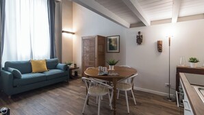 Ein Wohnzimmer mit einem blauen Sofa, einem Holzesstisch mit Stühlen, einer kleinen Pflanze und einer Wandskulptur.