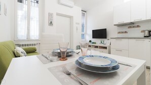 Eine moderne, gut beleuchtete Küche mit weißen Schränken, einem Esstisch gedeckt mit Tellern und Gläsern, und einem grünen Sofa im Hintergrund.