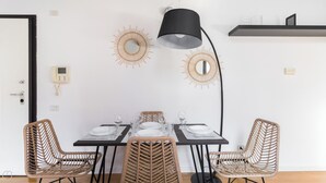 A dining area with a table set for four, surrounded by wicker chairs, a black floor lamp, and decorative sunburst wall art. - Italianway - Salomone 51 (Milan)