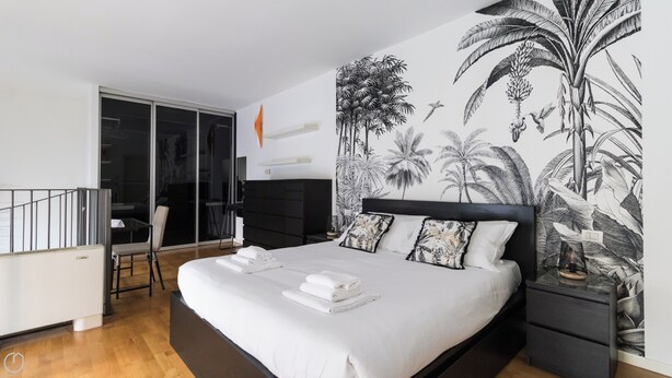 A modern bedroom with a large bed, a nightstand, and a wall mural of tropical plants. - Italianway - Salomone 51 (Milan)