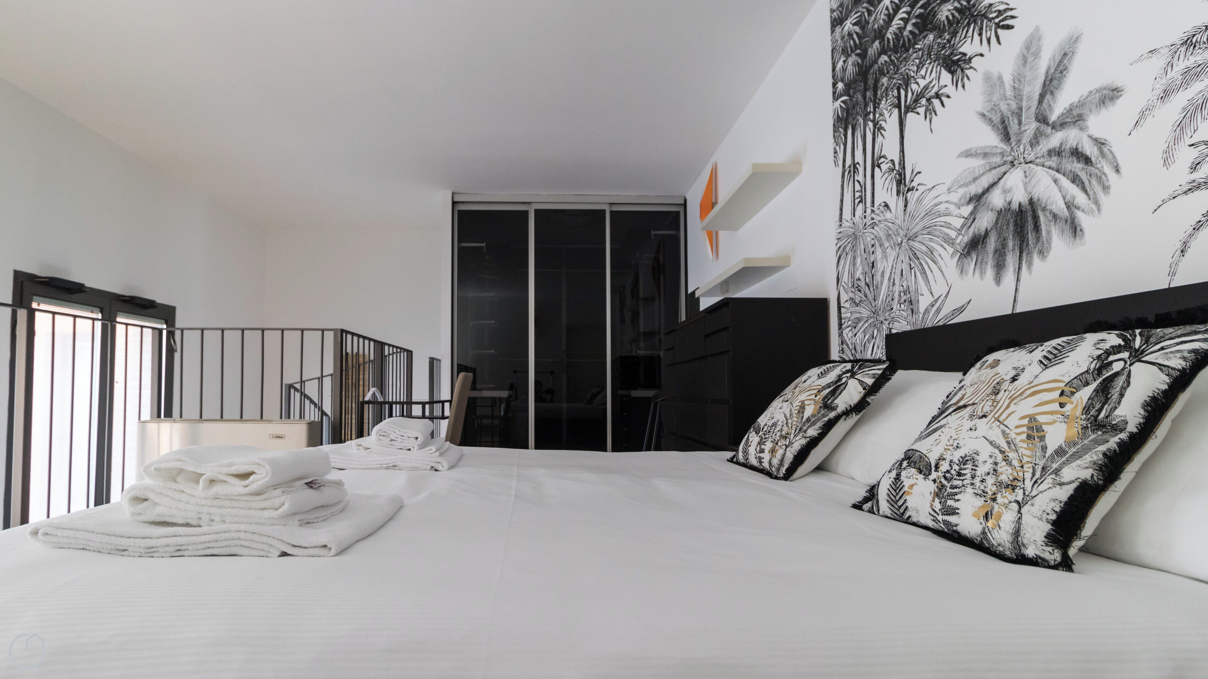 Una habitación de hotel moderna con una cama grande, vistas de la ciudad y un balcón con barandilla.