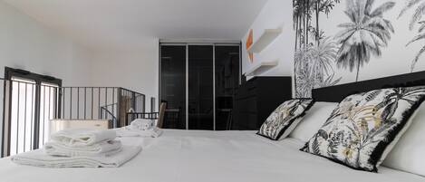 Una habitación de hotel moderna con una cama grande, vistas de la ciudad y un balcón con barandilla.