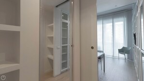 A modern interior with a walk-in closet, a dining area with a table and chairs, and a large window with curtains.