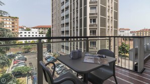 A balcony with a table and chairs, overlooking a parking area and buildings.