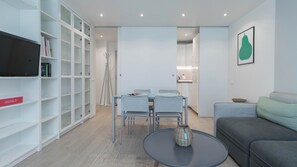 A modern living room with a grey sofa, a round coffee table, and a dining area with a glass table and metal chairs. There is a bookshelf with books and a framed picture on the wall. - Italianway - Sabotino 19 (Milan)