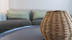 A wicker ottoman on a modern glass coffee table in a living room with a grey sofa and green cushions. - Italianway - Sabotino 19 (Milan)