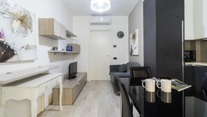 A modern kitchen with a black refrigerator, white cabinets, and a wooden countertop. There is a dining table with two mugs and a magazine.