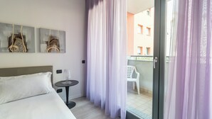 A hotel room with a bed, a small table with a lamp, and a balcony with a chair.