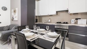 A modern kitchen with white cabinets, a dining table set for four, and a sofa in the adjacent living area.