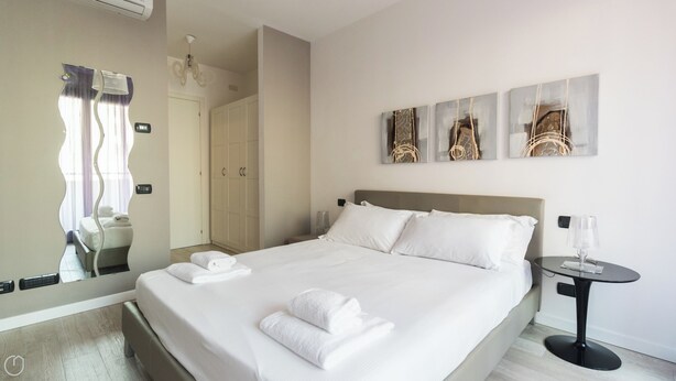 A hotel room with a large bed, a bedside table with a lamp, a wardrobe, and a mirror with a unique design.