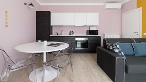 A compact kitchen with white cabinets, a microwave, and an oven. There is a dining table with chairs and a sofa with cushions. - Italianway Comfort - Buenos Aires 65 A (Milan)