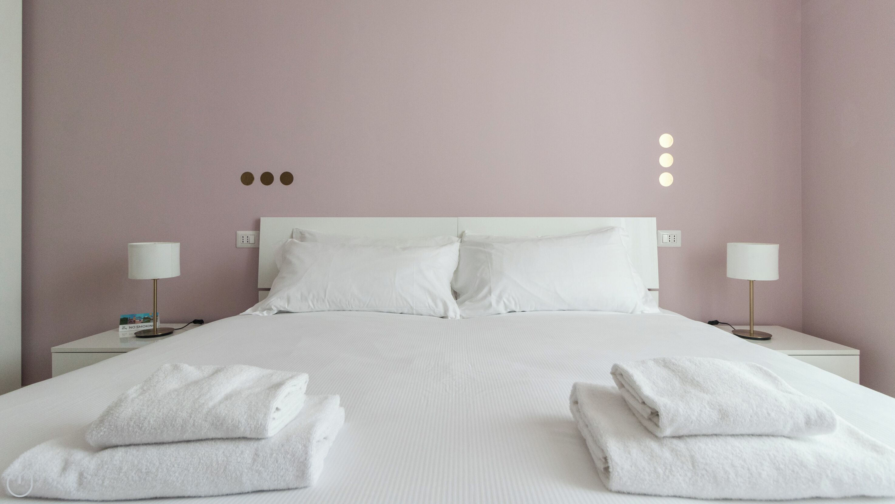 A neatly made bed with white linens, two bedside lamps, and folded towels on the nightstands.