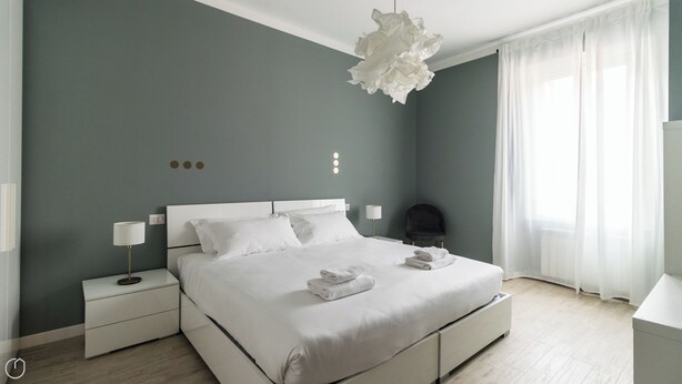 A modern bedroom with a large bed, bedside tables, a hanging light fixture, and a view of the outdoors through sheer curtains. - Italianway Comfort - Buenos Aires 65 A (Milan)