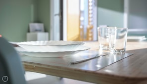 A dining table with a white plate, two glasses, and a spoon.