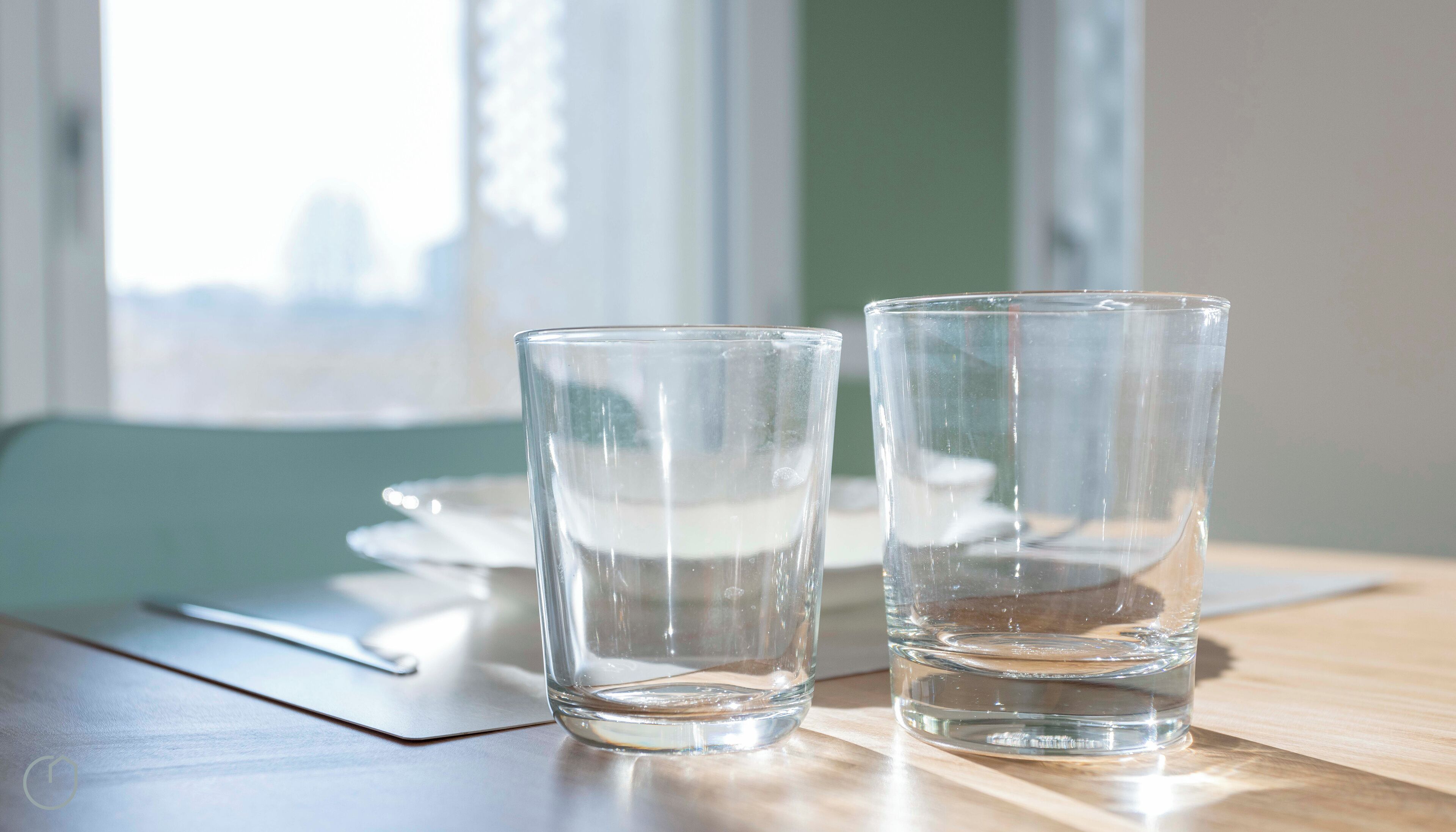 Two clear glasses on a wooden table with a napkin and a spoon beside them.