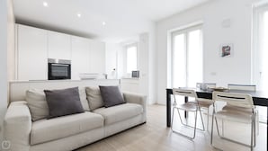 A modern kitchen with white cabinets, a built-in oven, and a dining area with a table and chairs. - Italianway - Spontini 10 (Milan)