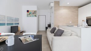 A modern living room with a white sofa, a flat-screen TV, and a dining area with a table and chairs. - Italianway - Spontini 10 (Milan)