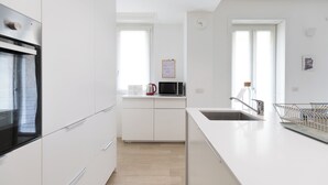 A modern kitchen with white cabinetry, a stainless steel oven, a microwave, and a sink with a stainless steel faucet. - Italianway - Spontini 10 (Milan)