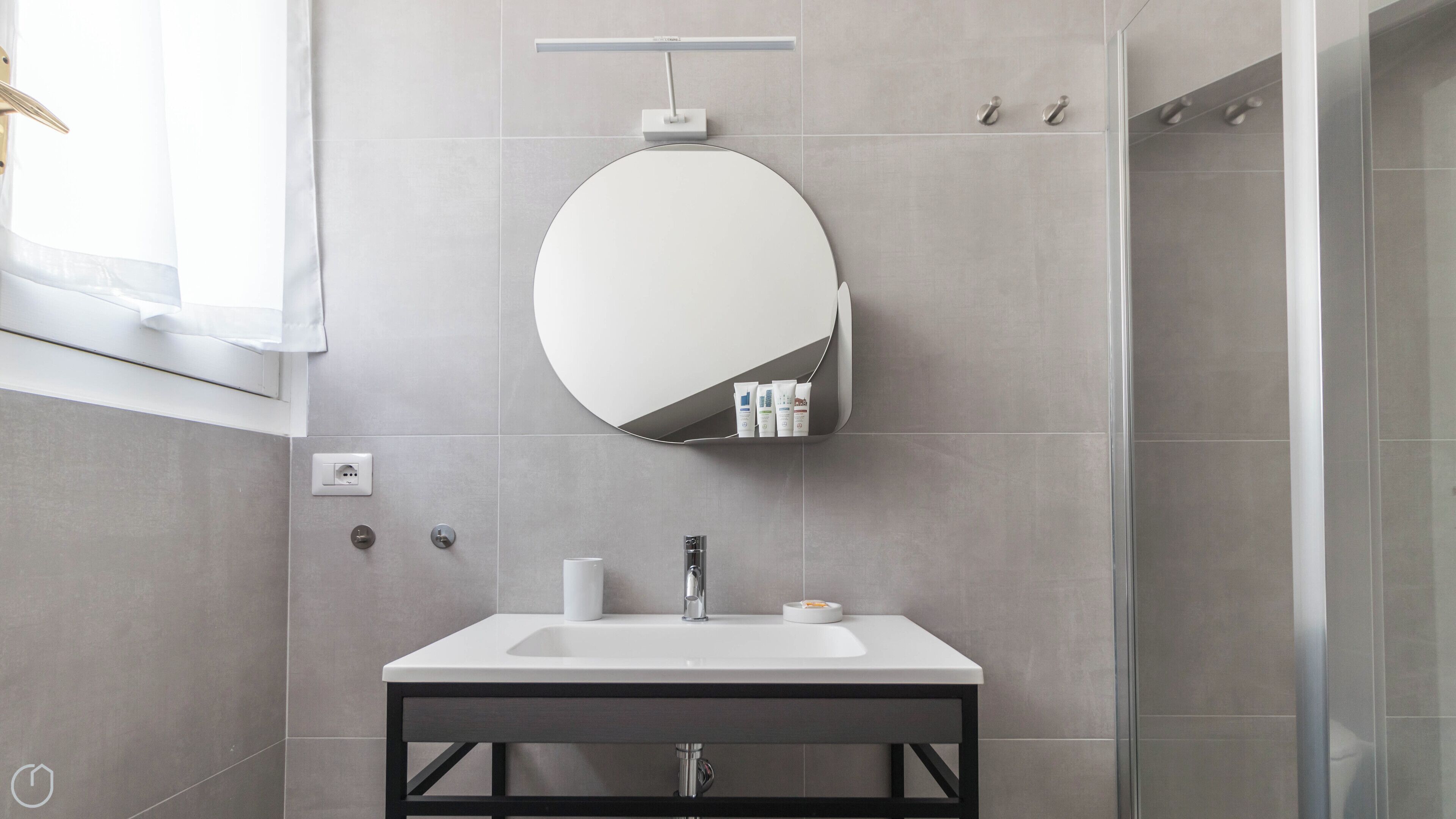 A modern bathroom with a round mirror, a white sink, and a glass shower enclosure.
