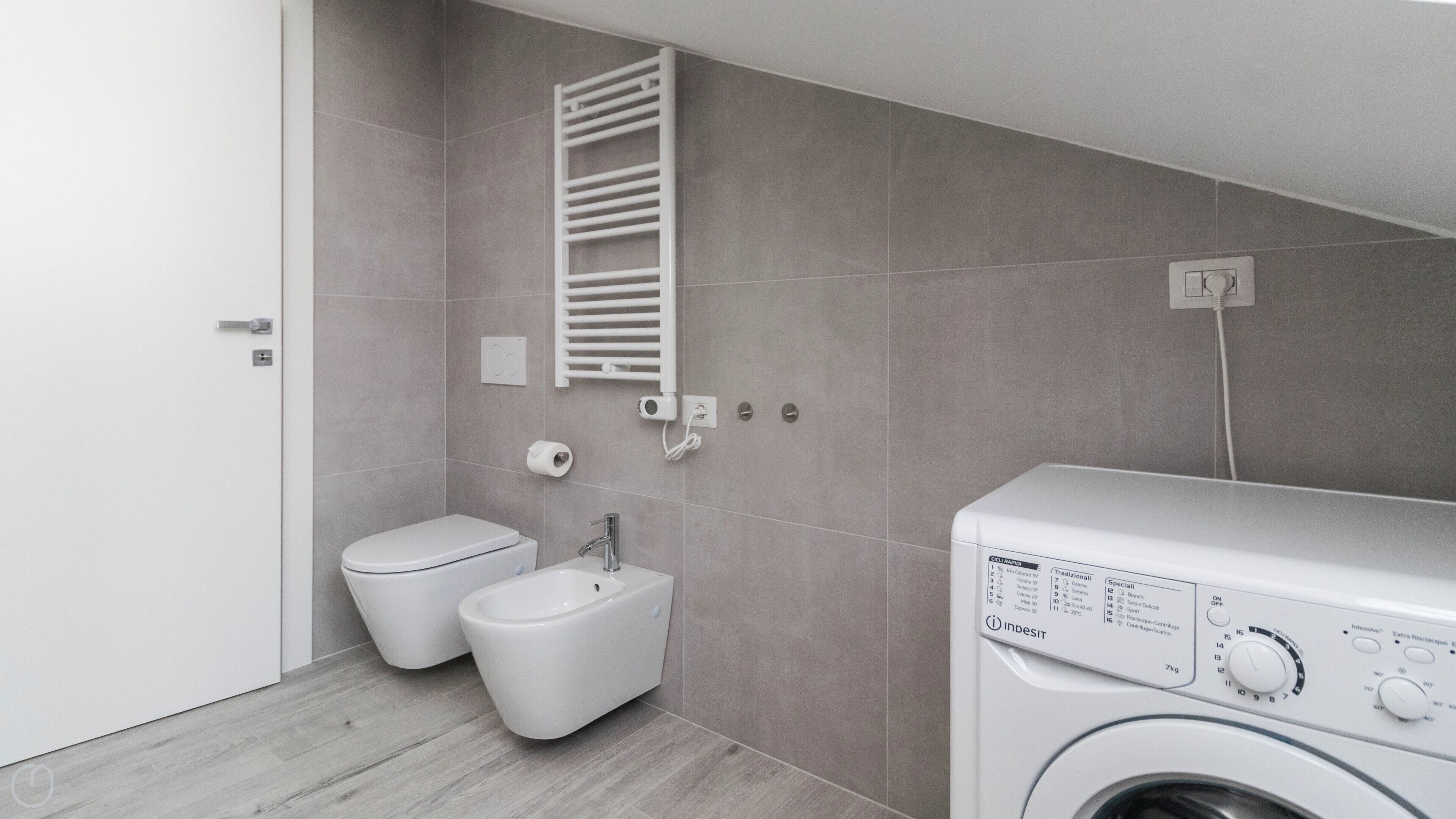 A modern bathroom with a toilet, bidet, sink, and a washing machine.