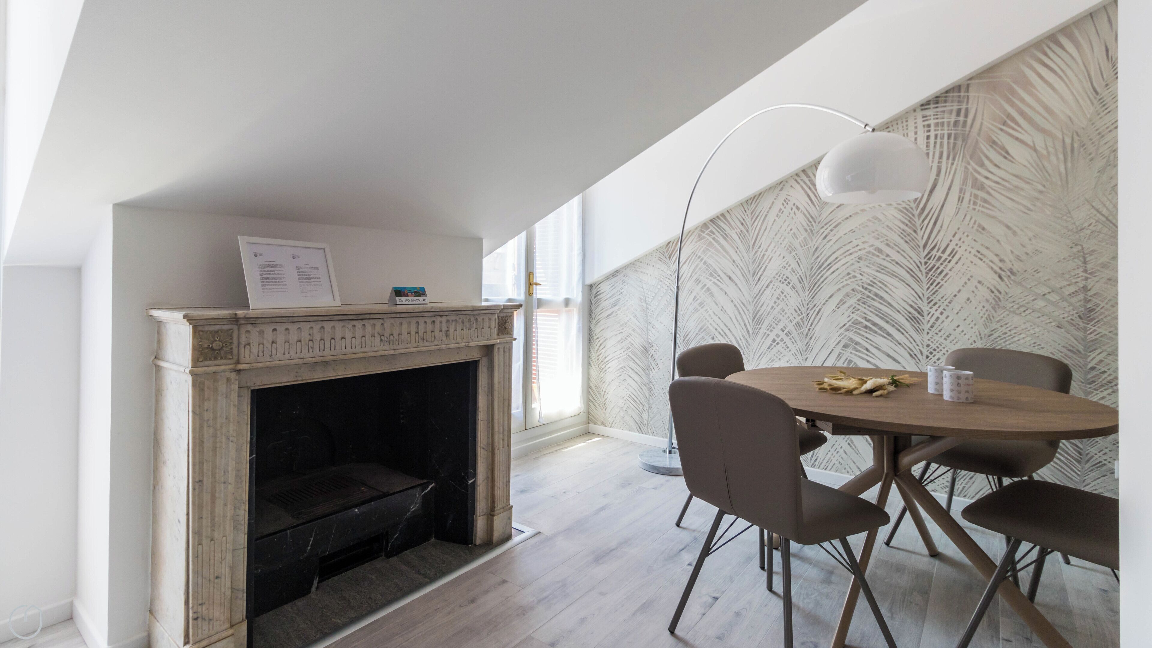 Un espace repas moderne avec une table ronde, quatre chaises, une cheminée et un mur décoré d’un motif.