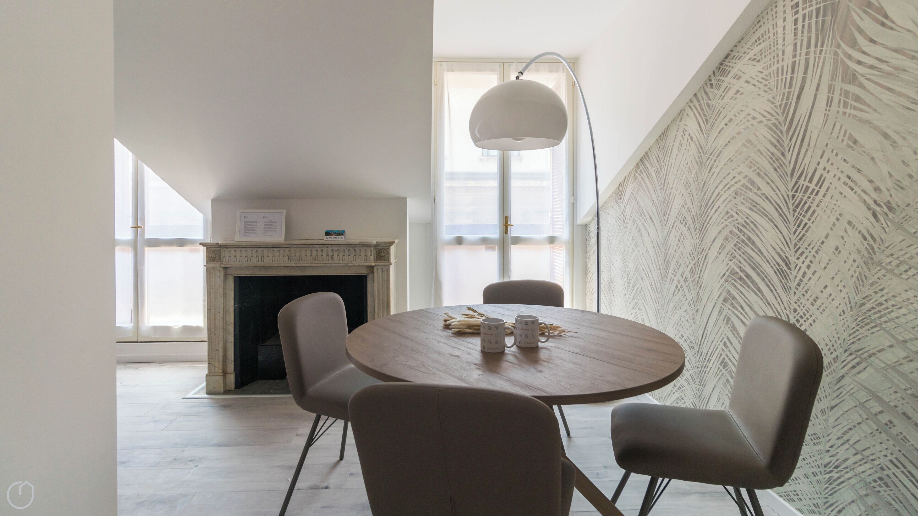 A modern dining area with a round wooden table, four chairs, a fireplace, and a large window with a view.