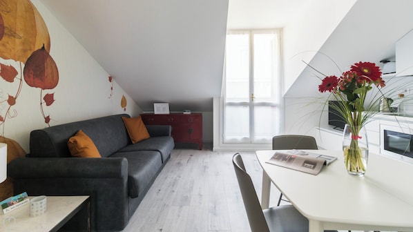 Una sala moderna con un sofá gris, una mesa de comedor con un jarrón de flores y un mueble rojo al fondo.