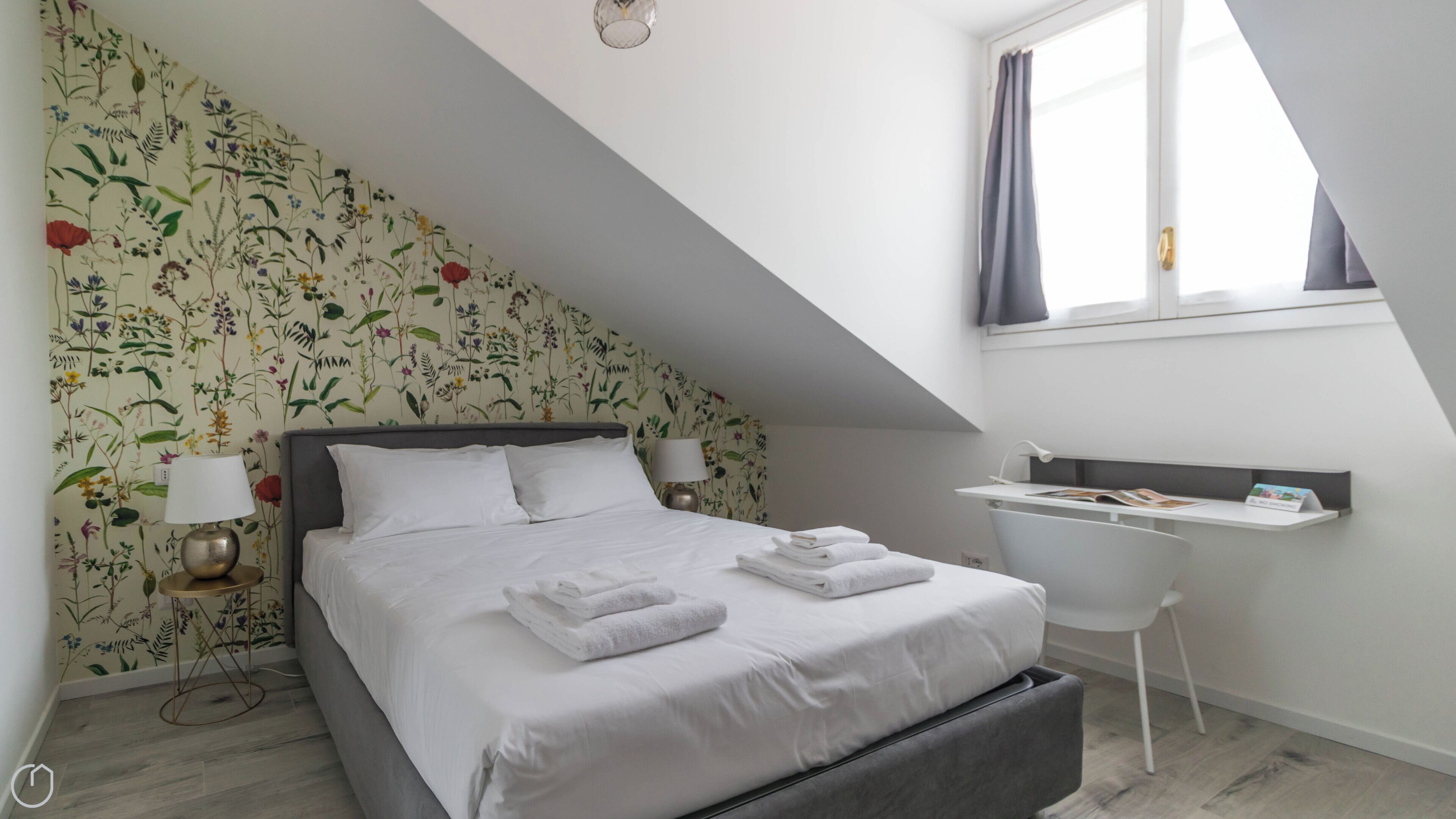 Ein Schlafzimmer mit einem Bett, zwei Nachttischlampen, einem Schreibtisch und einem Fenster mit Vorhängen.