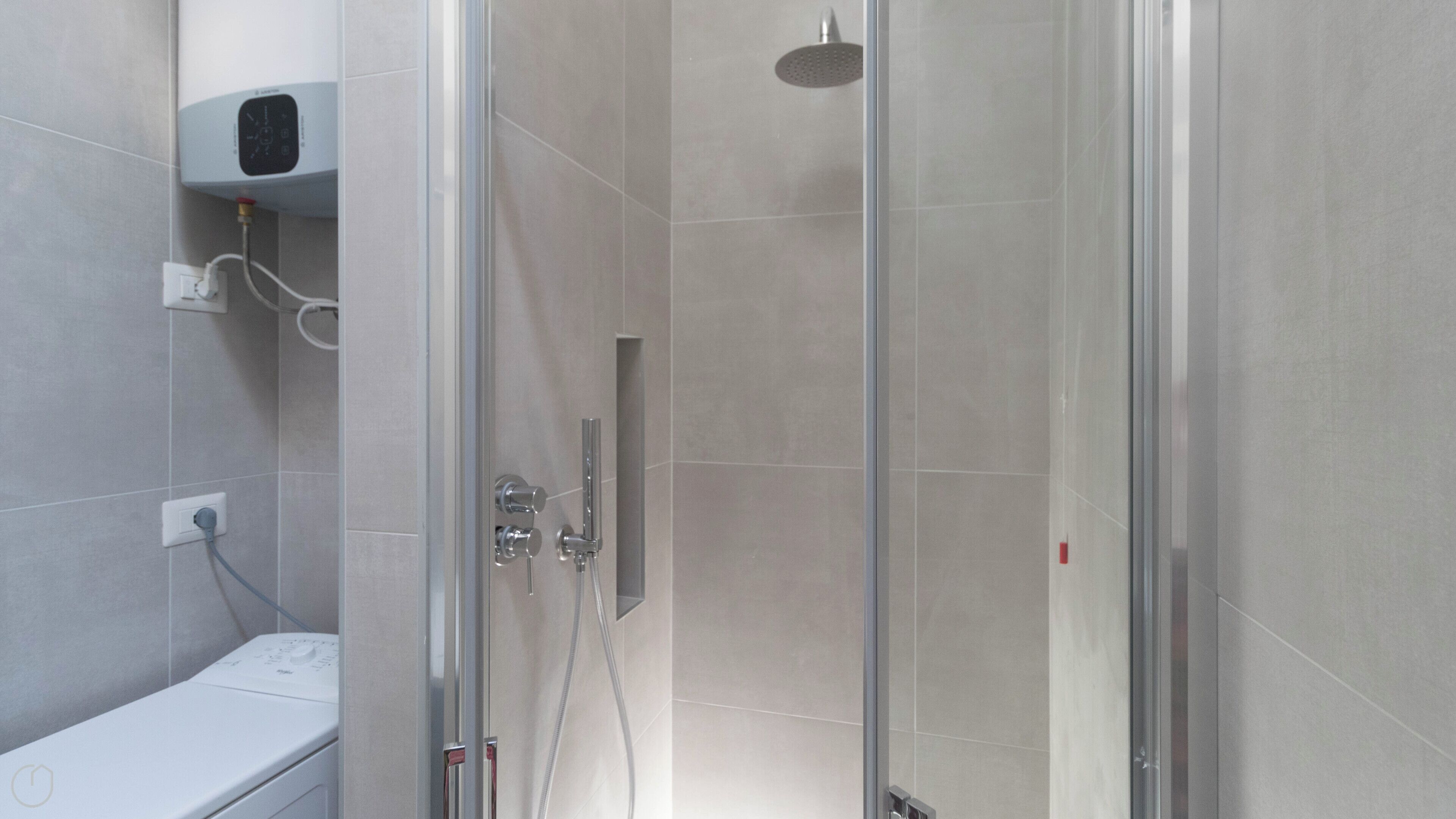Een moderne douche met een glazen deur, een handdouche en een bedieningspaneel aan de muur.