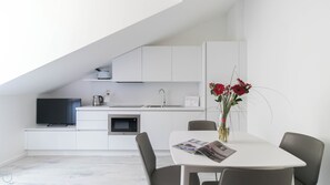 Una cocina moderna con armarios blancos, horno empotrado y un lavabo. Hay una mesa de comedor con sillas y un florero con flores rojas.
