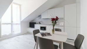 Una cocina moderna con armarios blancos, un comedor con mesa y sillas blancas, y un ventanal que proporciona luz natural.