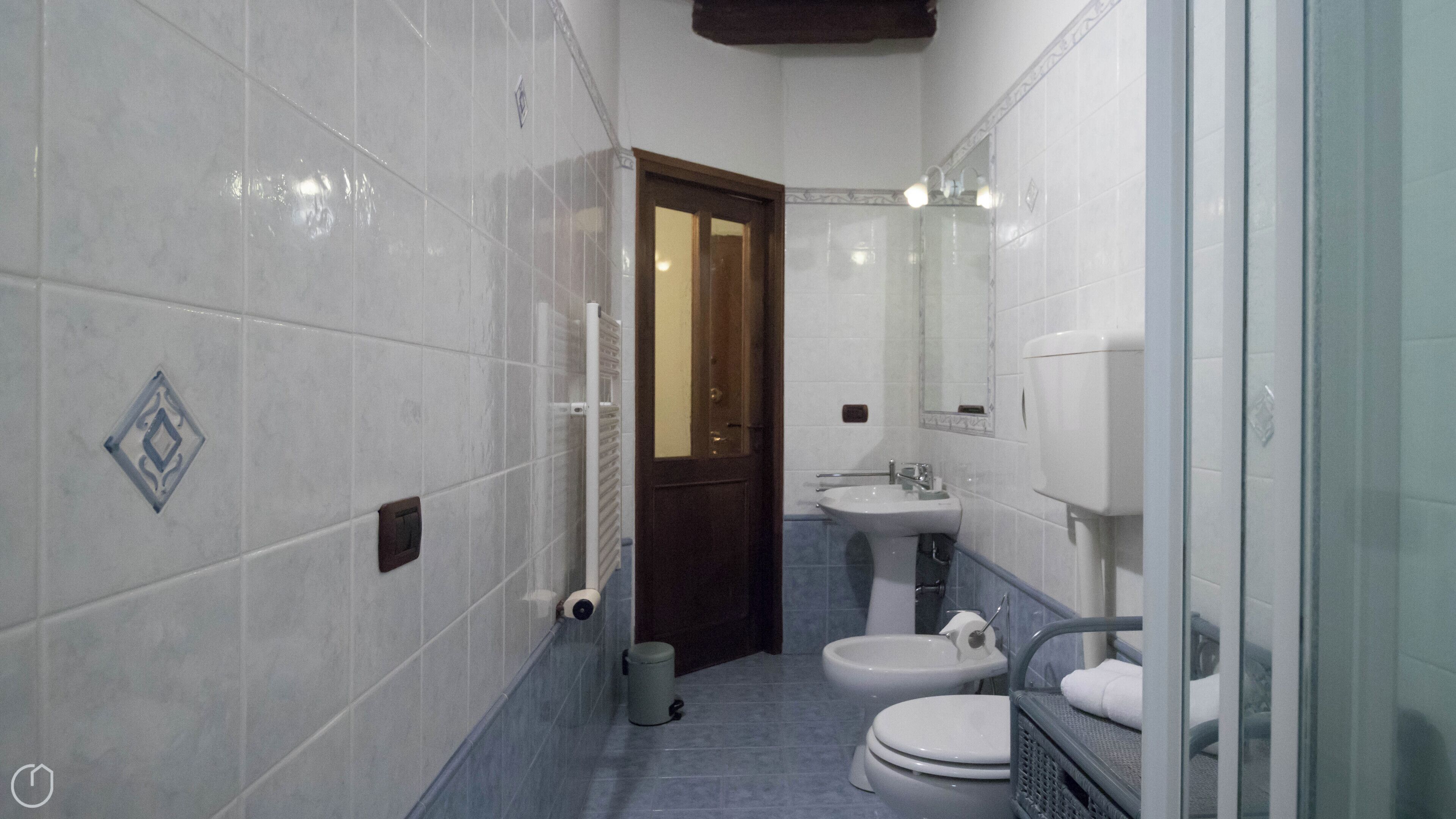 A bathroom with white tiled walls, a sink, a toilet, and a shower area.