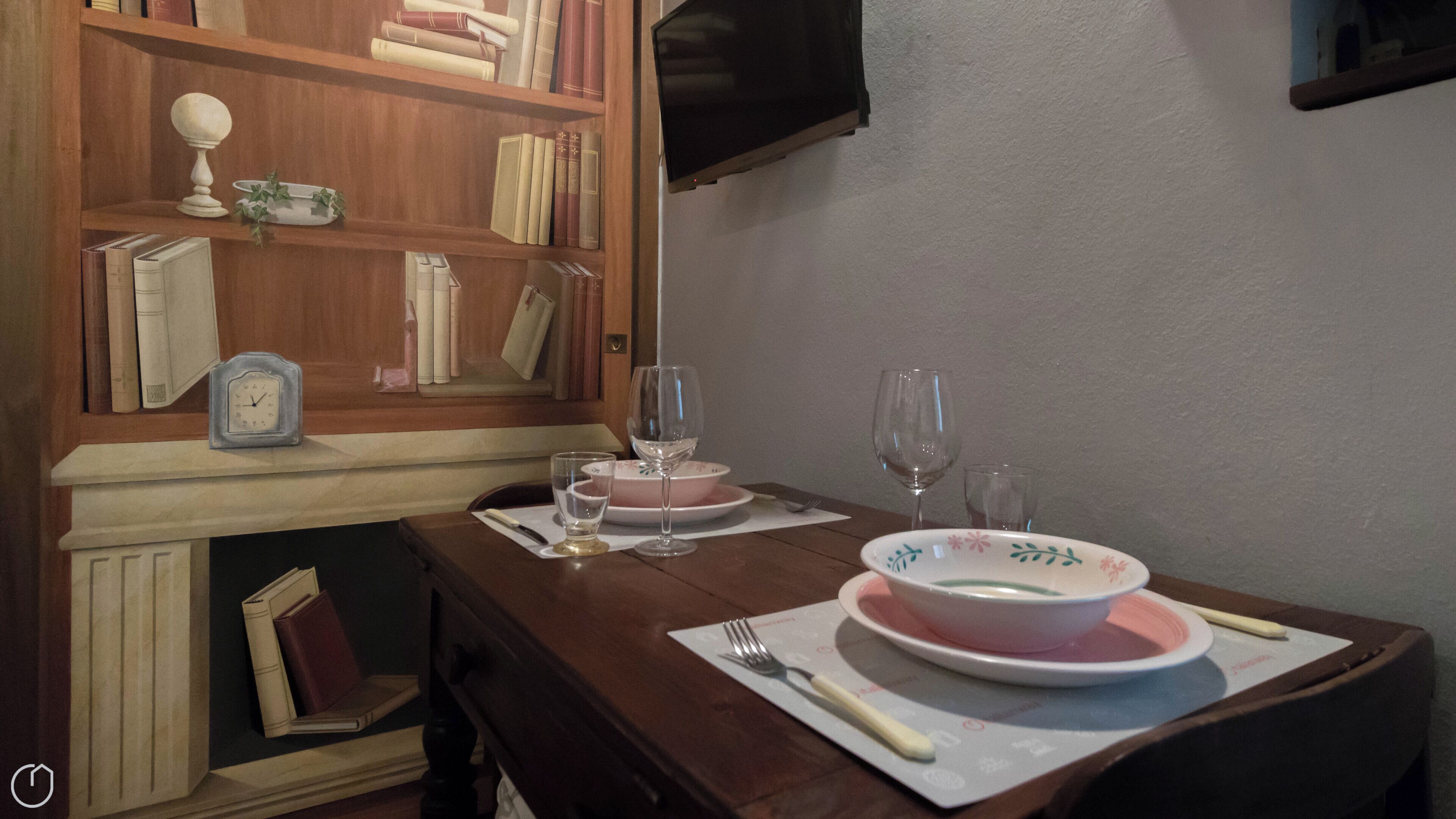 Un tavolo da pranzo con un piatto rosa e bianco, un bicchiere da vino, una forchetta e una sveglia.