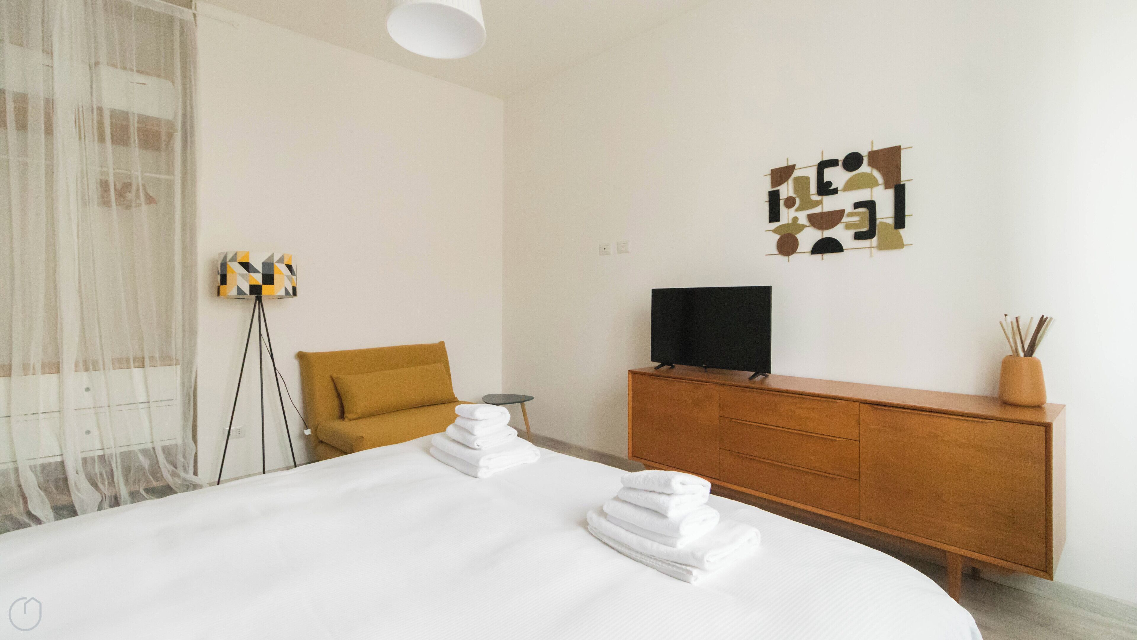 A hotel room with a large bed, a wooden dresser, a television, and a decorative wall piece.