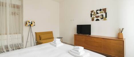 A hotel room with a large bed, a wooden dresser, a television, and a decorative wall piece.