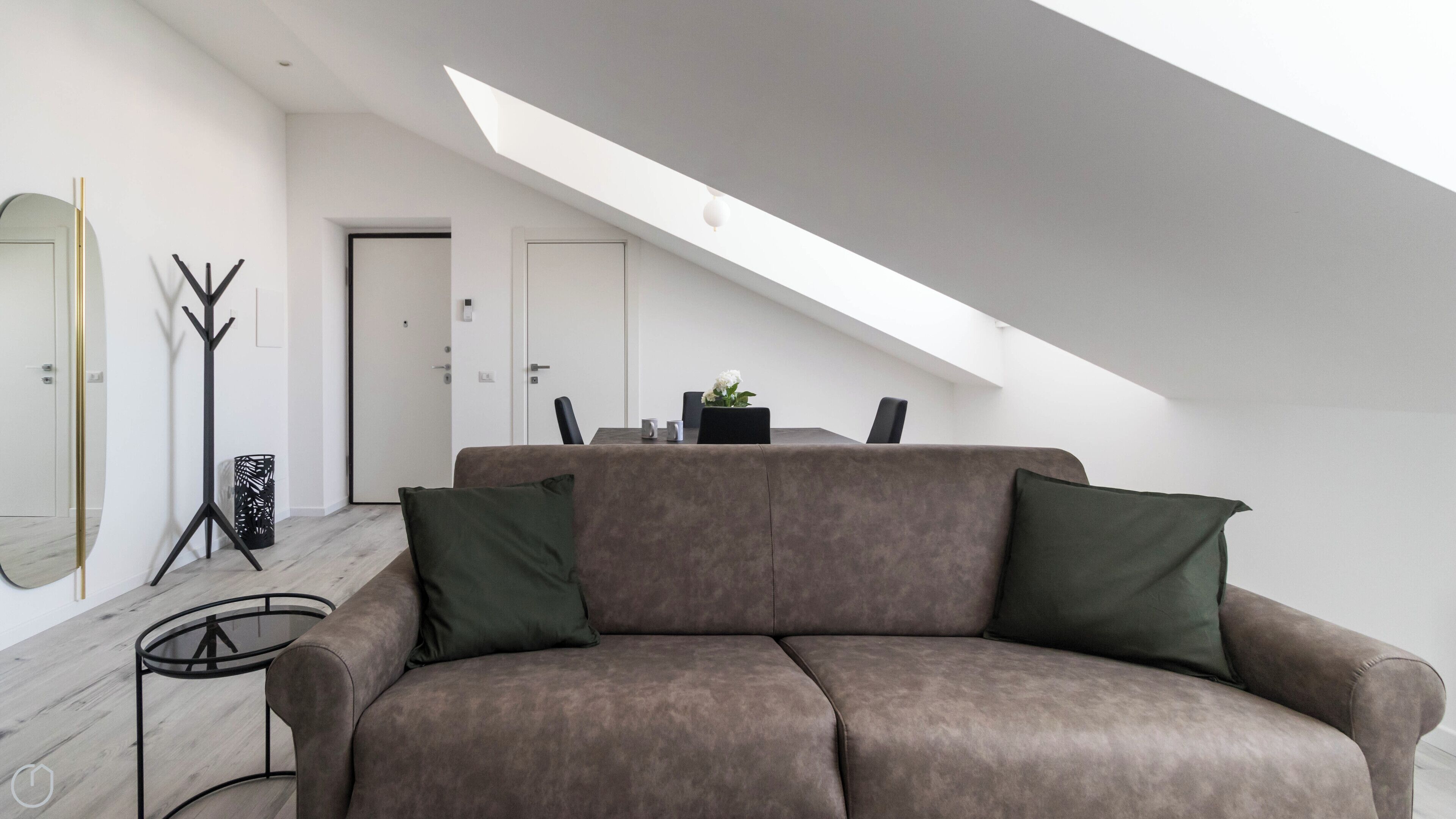 Un loft moderno con techos altos, un sofá marrón con cojines verdes, una mesa de comedor con sillas y un espejo grande en la pared.