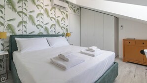 A neatly made bed with white linens and folded towels, a green headboard, and a wall with a palm tree wallpaper. - Italianway - Commenda 35 C (Milan)
