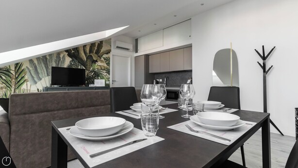 A modern dining area with a dark table set for four, white plates, clear glasses, and a black chair. - Italianway - Commenda 35 C (Milan)