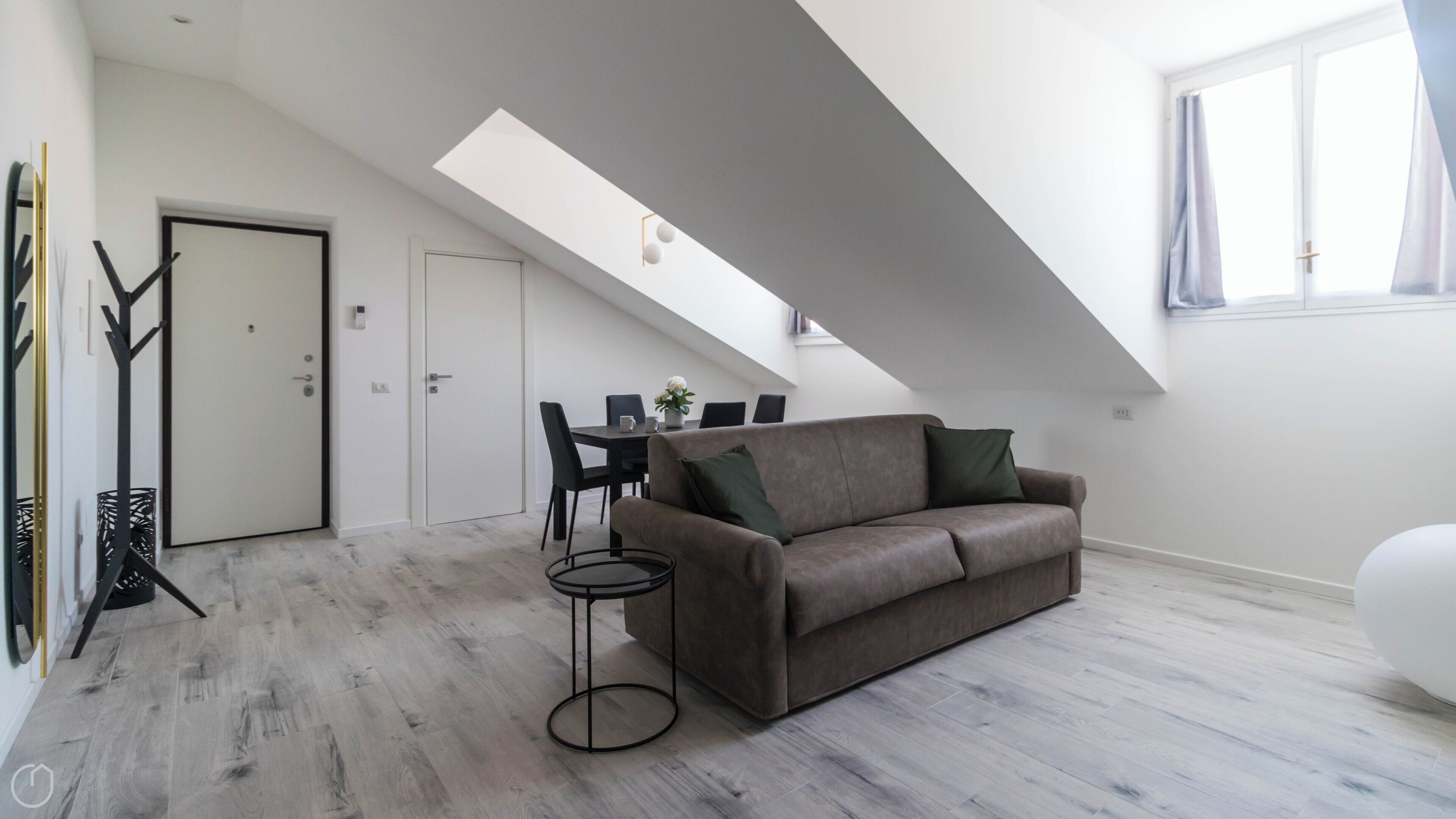 En modern lägenhet i loftstil med högt i tak, en matplats och ett vardagsrum med en brun soffa och ett litet runt bord.